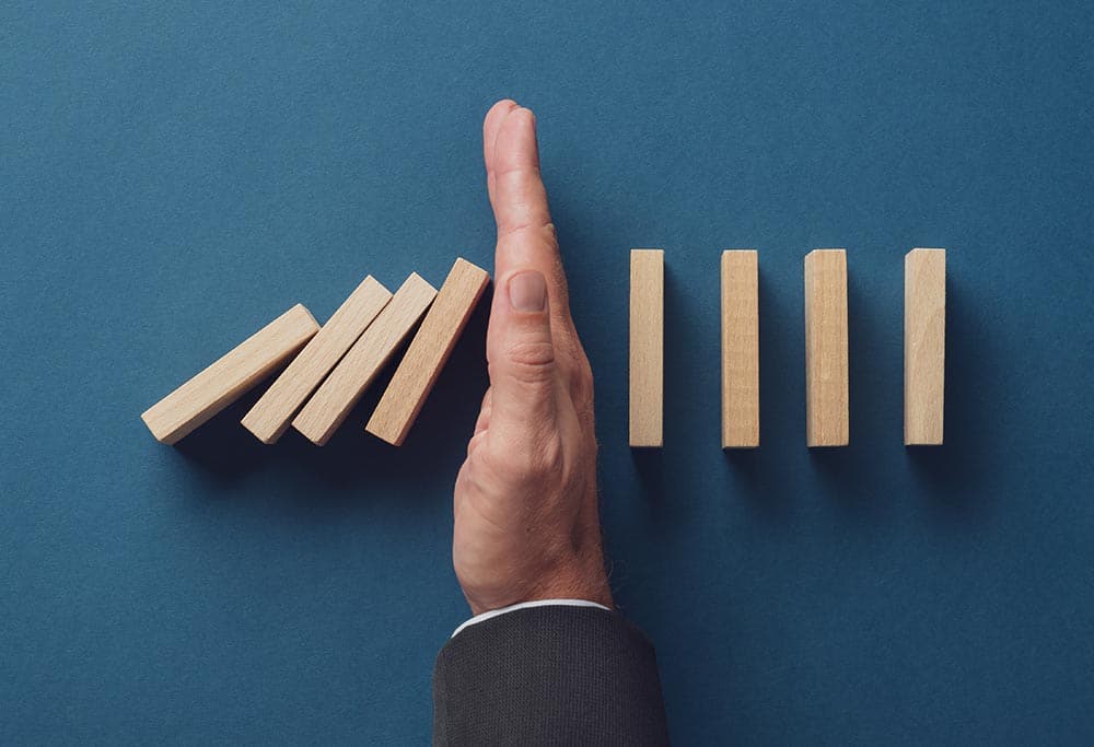 Business crisis manager stopping falling dominos from collapsing